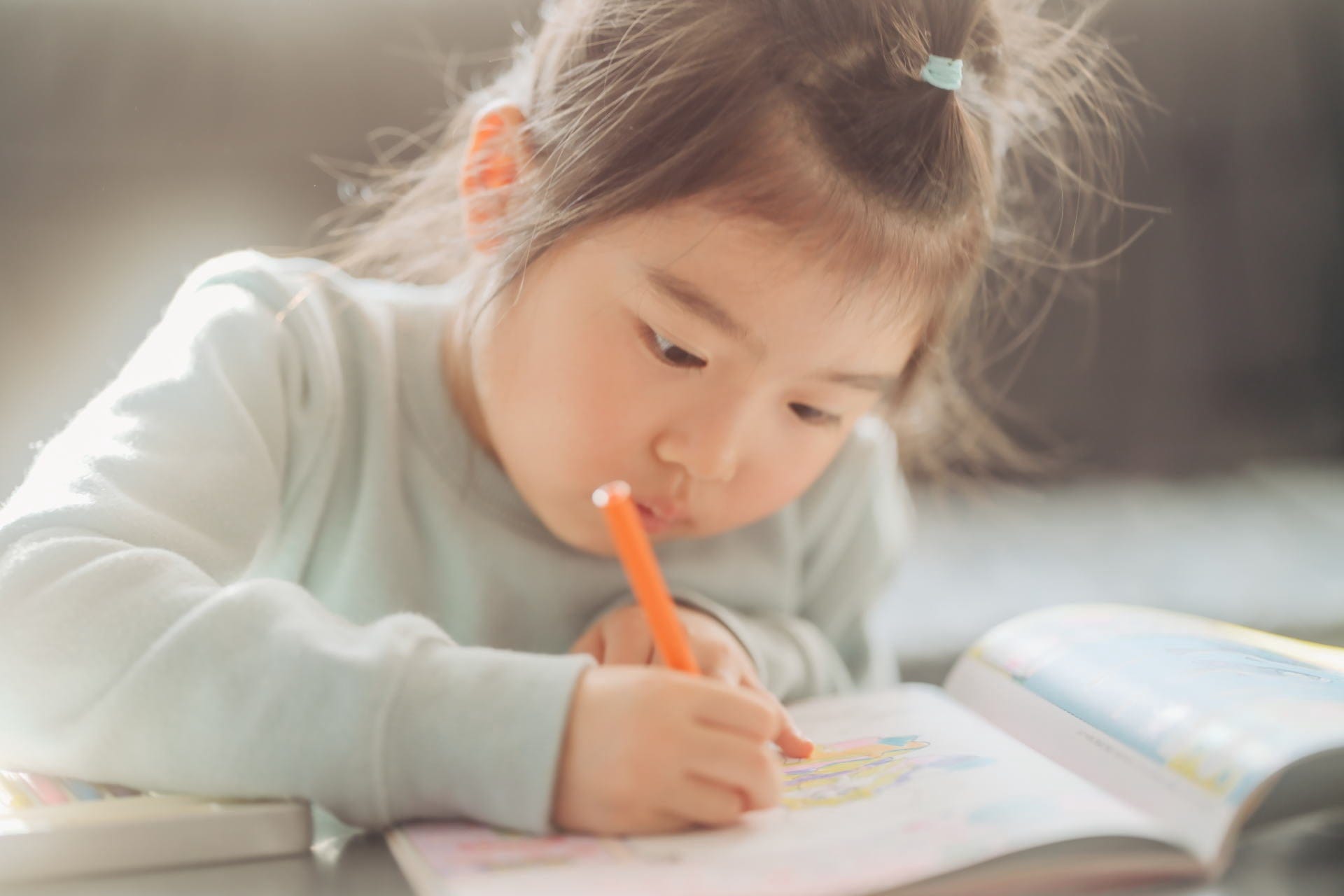 机に向かい鉛筆を握る幼い子ども