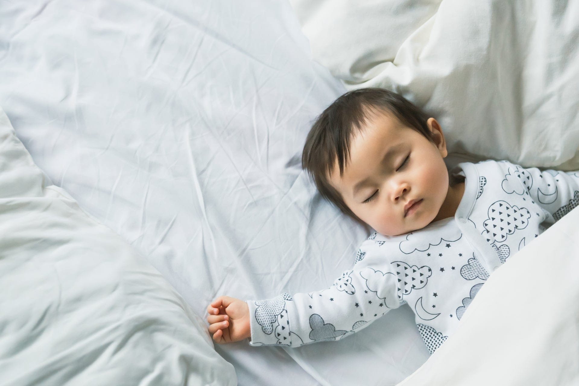白い寝具に包まれて眠る赤ちゃん